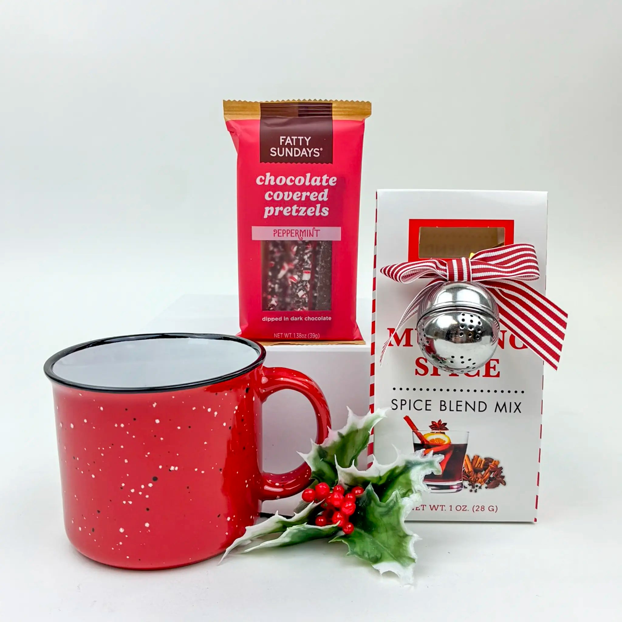 Red mug with a package of Fatty Sundays chocolate covered pretzels and a box of Moxie Spice spice blend mix on a white background.