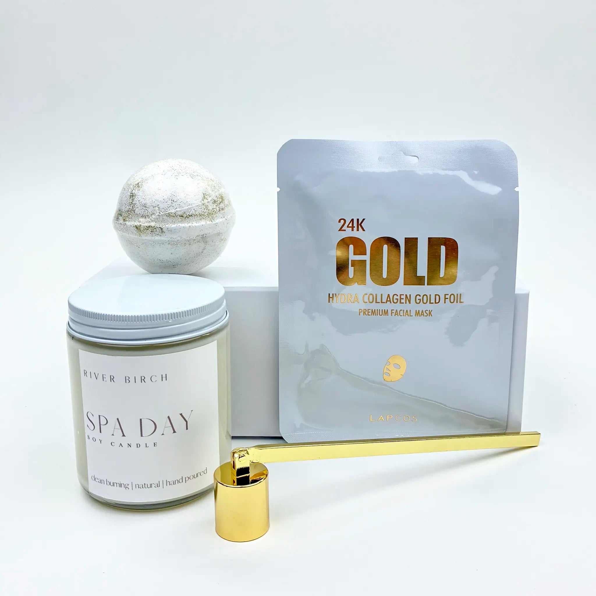 Spa Day candle, gold foil pack, and a gold candle snuffer on a white background