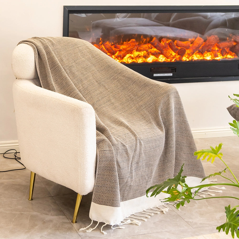 Beige armchair with a textured blanket draped over it, in front of an electric fireplace.