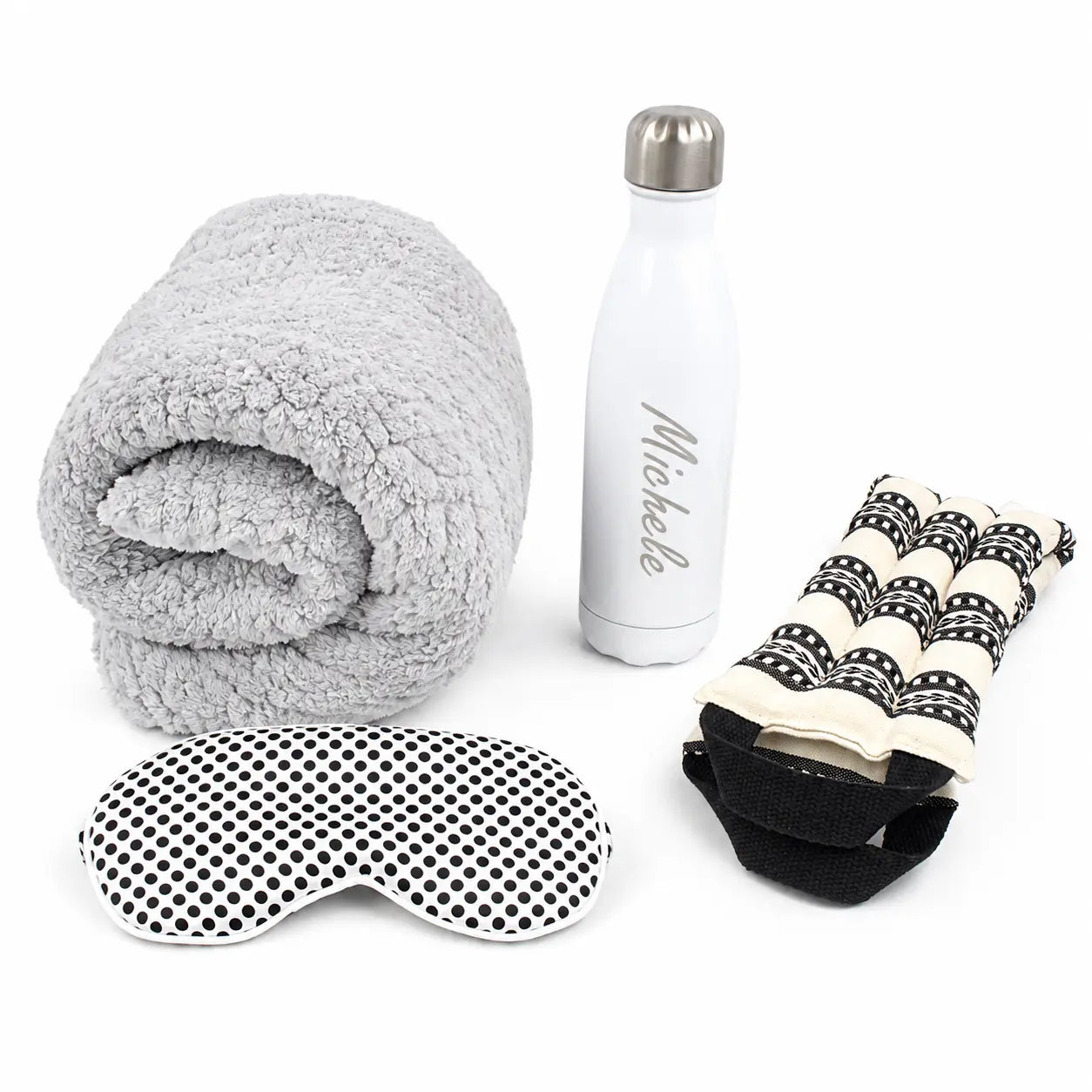 A travel wellness set featuring a gray sherpa fleece blanket, a white insulated water bottle with a silver cap and 'Mikelle' printed on it, a black-and-white polka dot eye mask, and a cream-and-black patterned neck pillow.