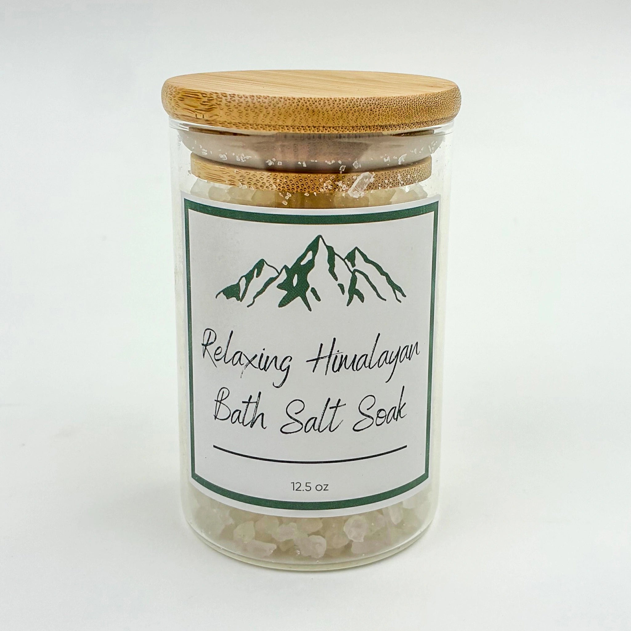 Glass jar of relaxing Himalayan bath salt soak with a wooden lid on a white background
