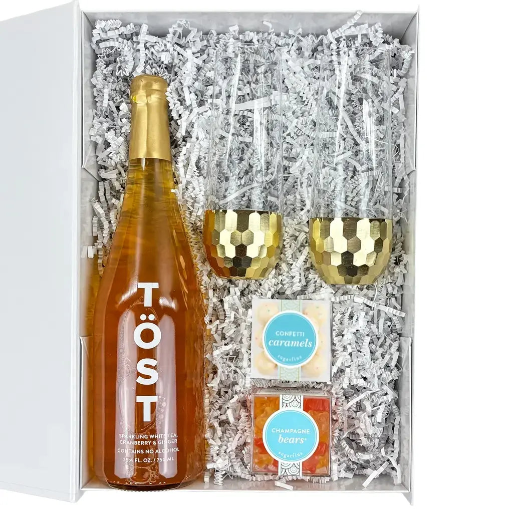 Gift set with a bottle of Töst sparkling wine, two gold flutes, and two boxes of candy in a white box.