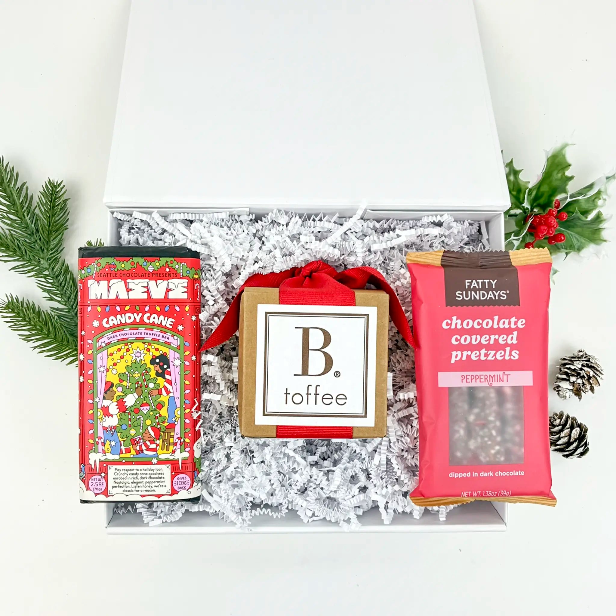 Gift box with festive treats including candy canes, toffee, and chocolate-covered pretzels on a white background.
