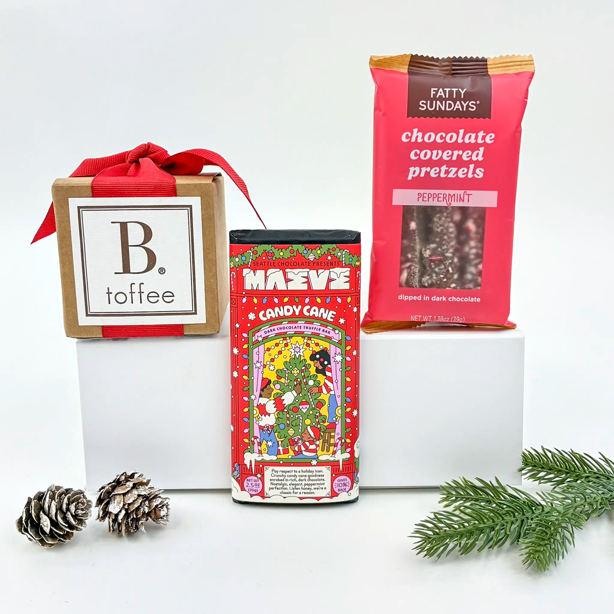 Assorted holiday-themed snacks including Fatty Sundays chocolate covered pretzels and Maeve candy canes on a white background.