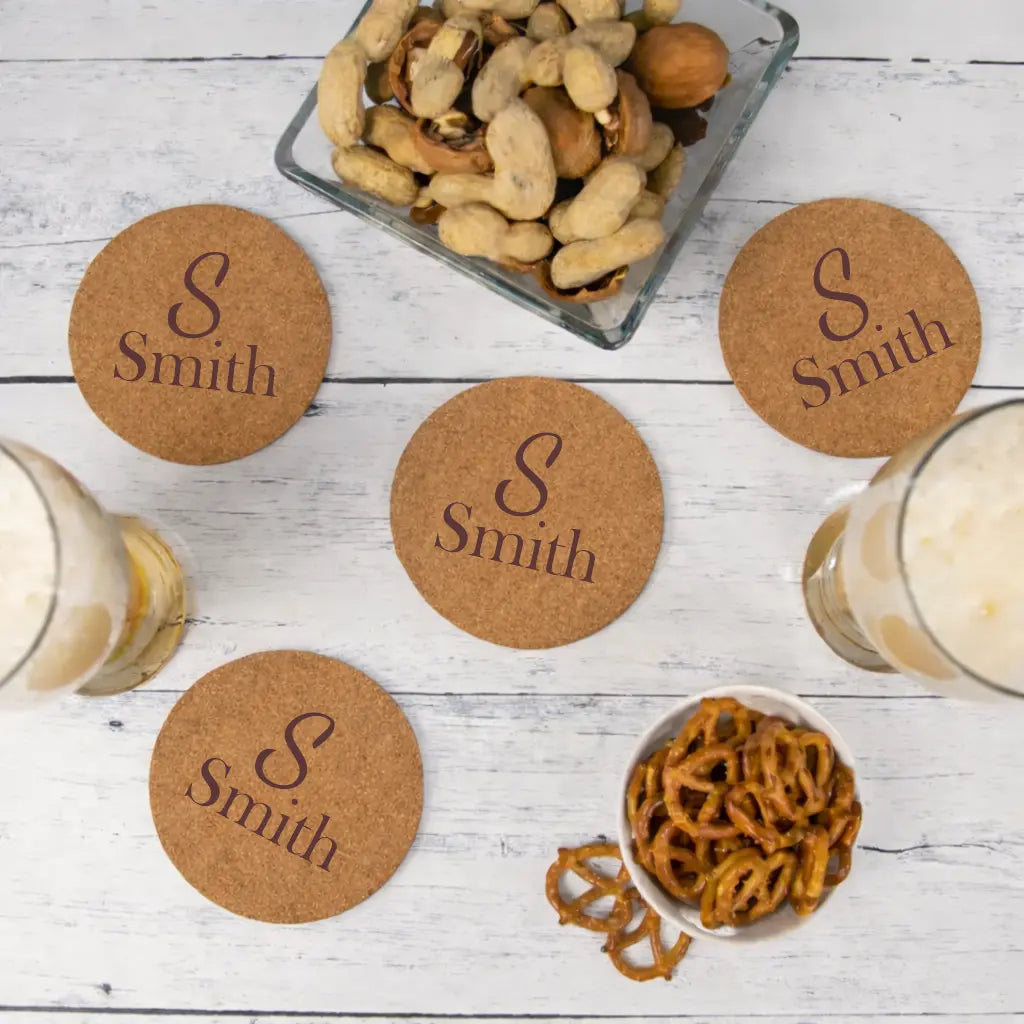 Cork coasters with 'S Smith' engraving on a wooden surface with snacks and drinks.
