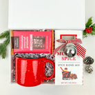 Holiday gift set with red mug, spice blend mix, and chocolate-covered pretzels on a white background.