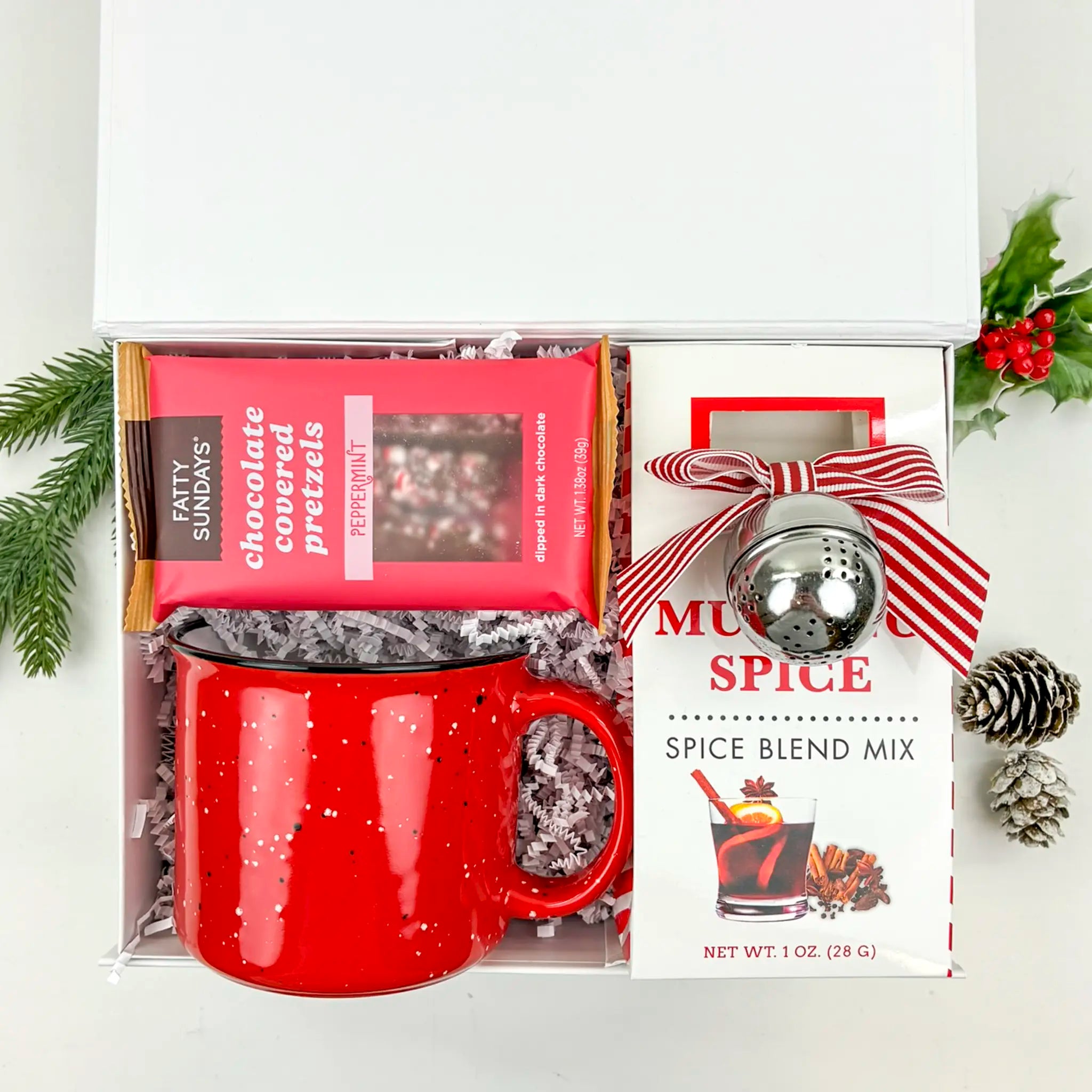Holiday gift set with red mug, spice blend mix, and chocolate-covered pretzels on a white background.