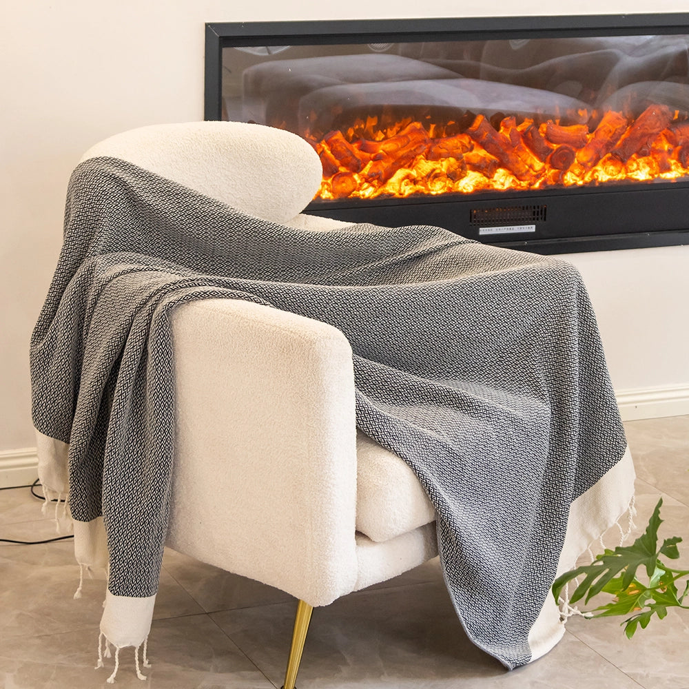 Beige armchair with a gray blanket draped over it, in front of a fireplace with visible flames.