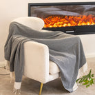 Beige armchair with a gray blanket draped over it, in front of a fireplace with visible flames.