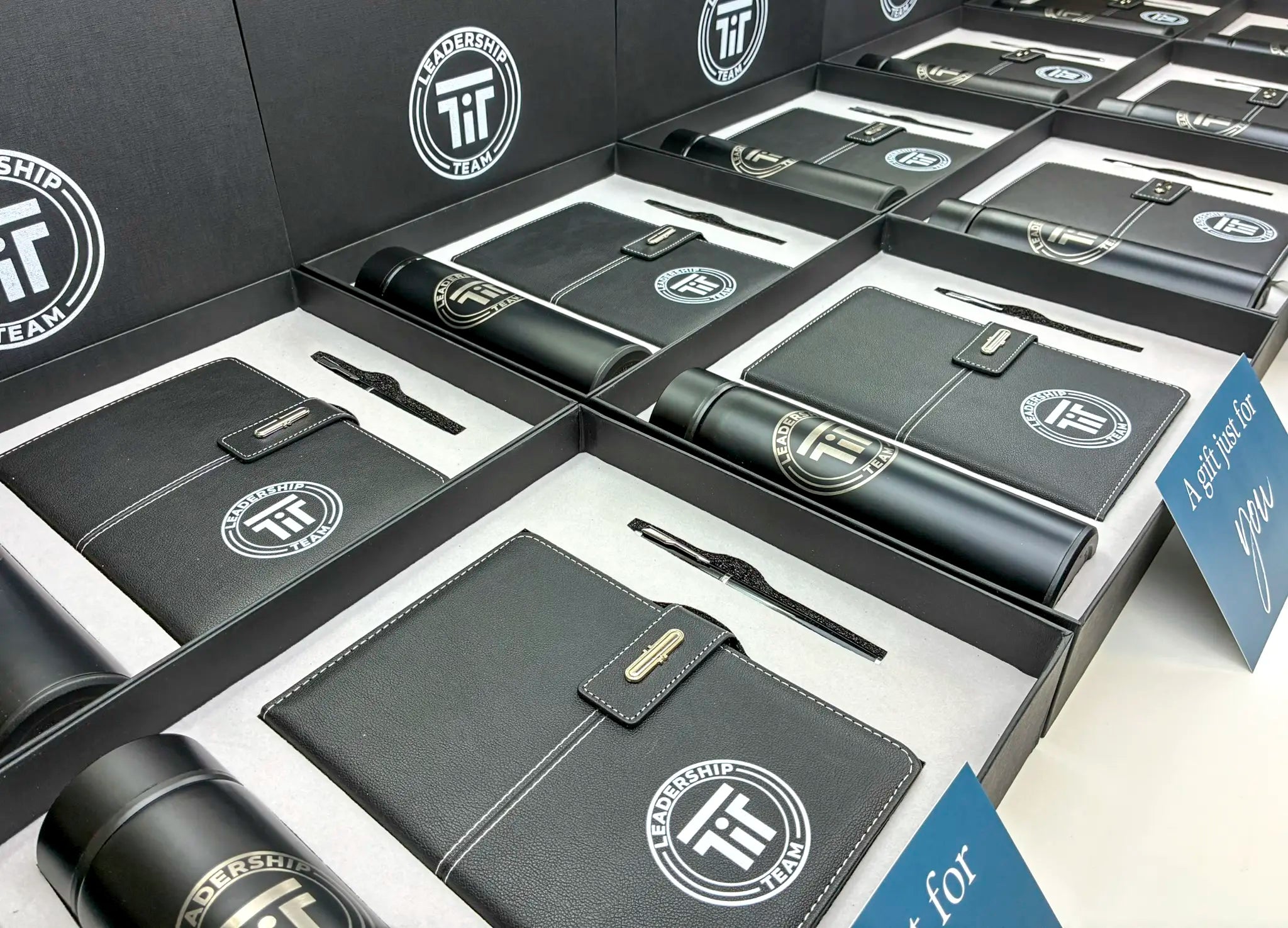 Black leather-bound notebooks with pen sets and visible logos in packaging on a white surface.
