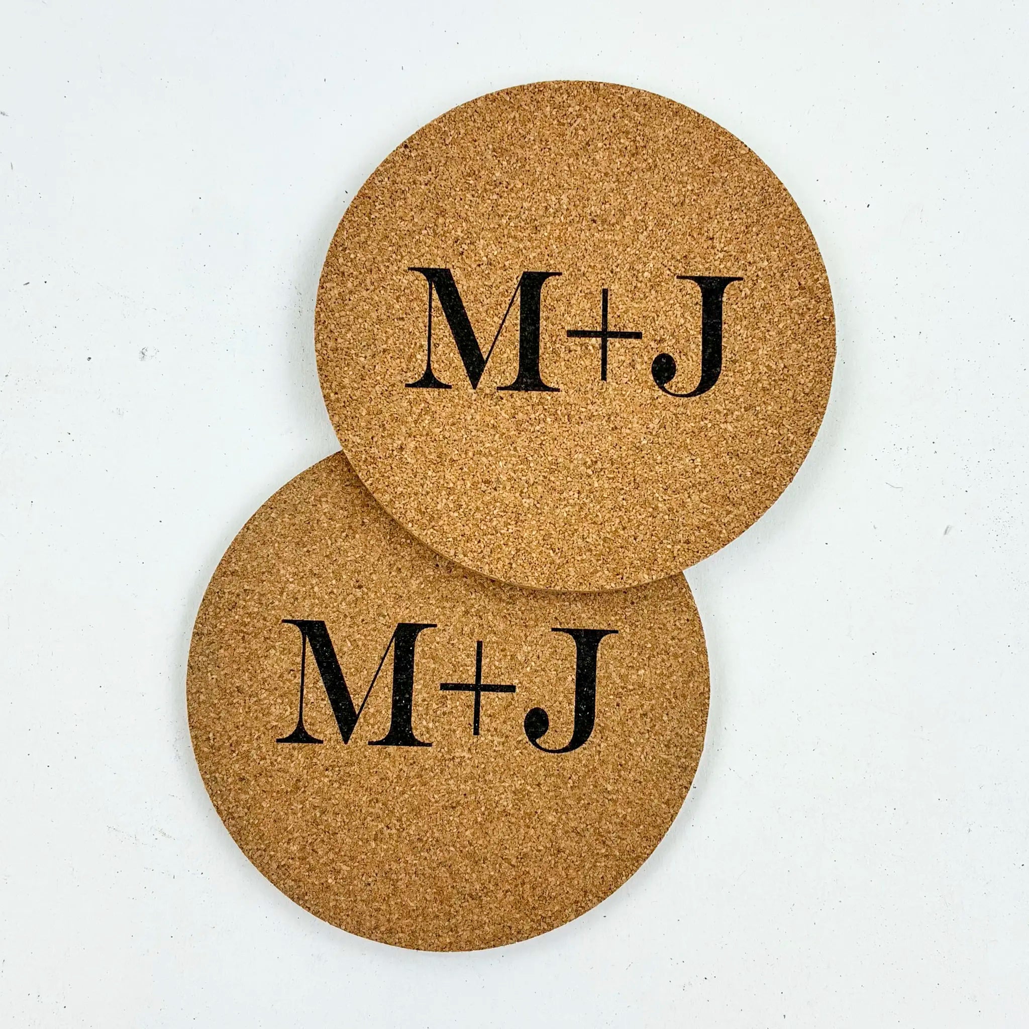 Two cork coasters with 'M+J' monogram on a white background