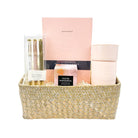 Gift basket with self-care items including candles, books, and stationery on a white background