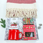 Gift set with a red mug, hot cocoa packets, and a blanket on a white background
