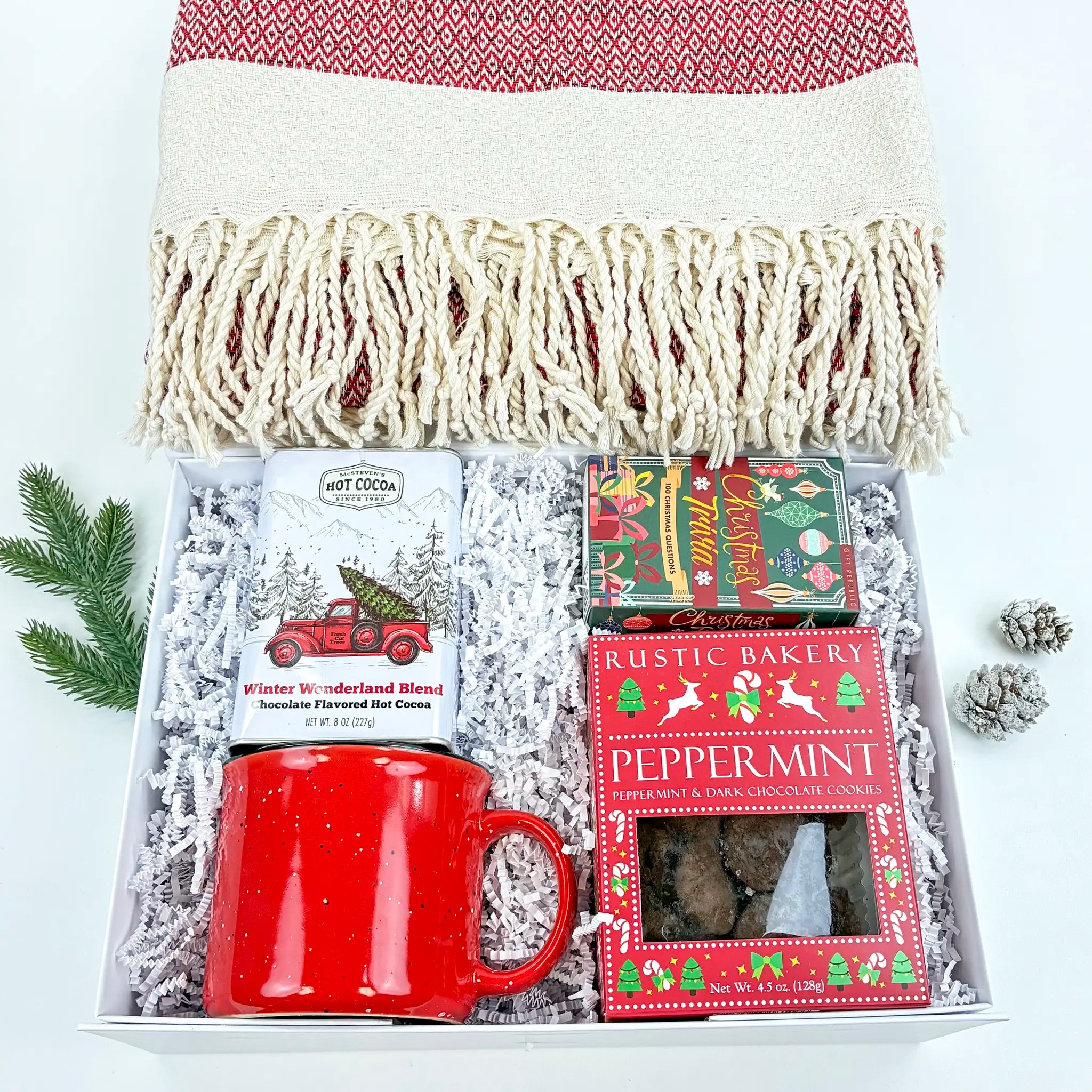 Gift set with a red mug, hot cocoa packets, and a blanket on a white background