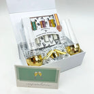 Gift set with gold tumblers, cocktail books, and a card inside a white box.