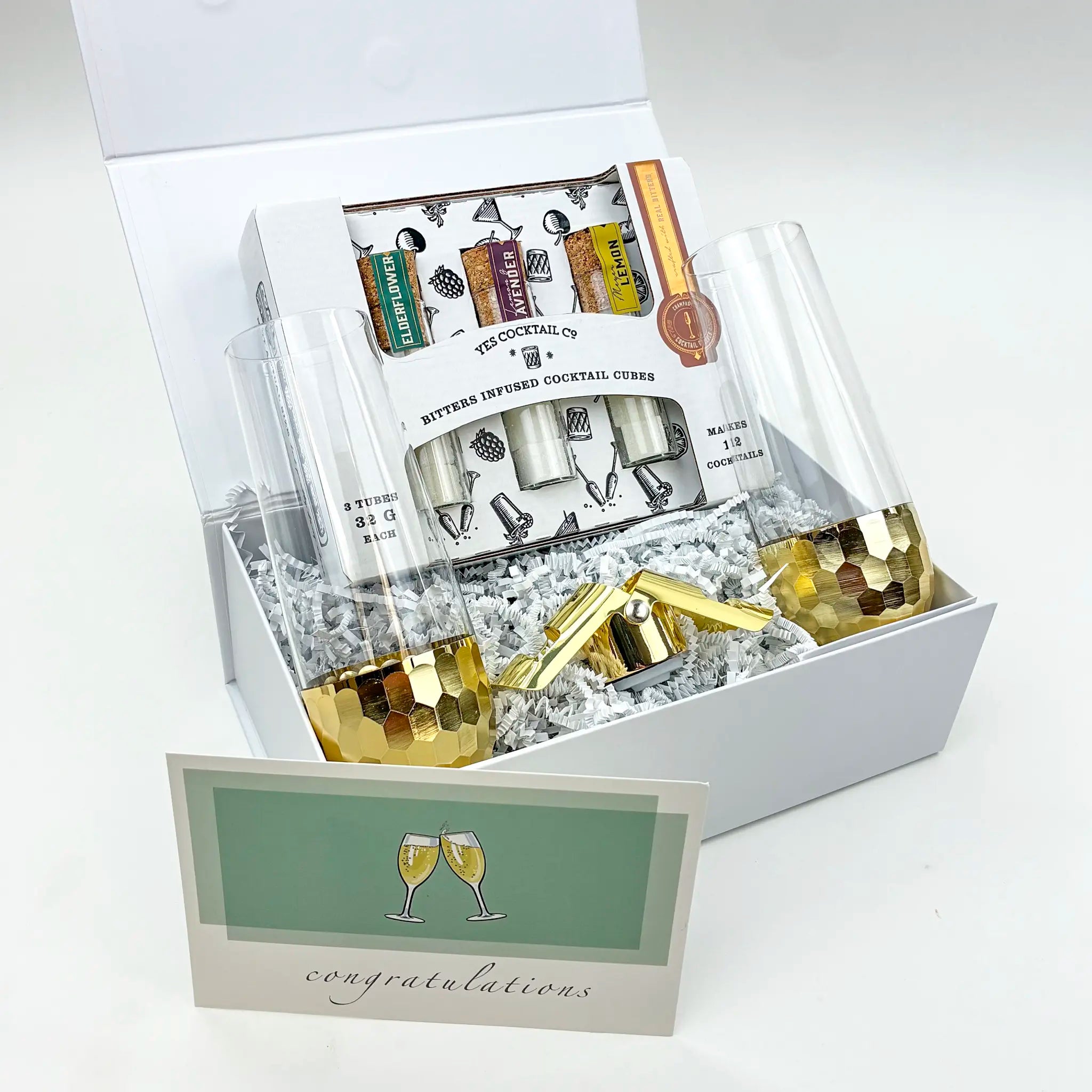 Gift set with gold tumblers, cocktail books, and a card inside a white box.