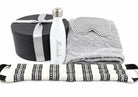 A curated gift set on a white background featuring a black round presentation box with a silver ribbon, a white insulated water bottle personalized with 'Michelle' in silver script, a folded gray plush towel, a gray and white polka-dot eye mask, and a black-and-white patterned neck pillow.