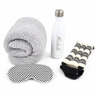 A travel wellness set featuring a gray sherpa fleece blanket, a white insulated water bottle with a silver cap and 'Mikelle' printed on it, a black-and-white polka dot eye mask, and a cream-and-black patterned neck pillow.
