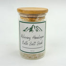 Glass jar of relaxing Himalayan bath salt soak with a wooden lid on a white background