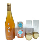 Bottle of Töst sparkling white tea, two glasses with gold bases, and a small box on a white background