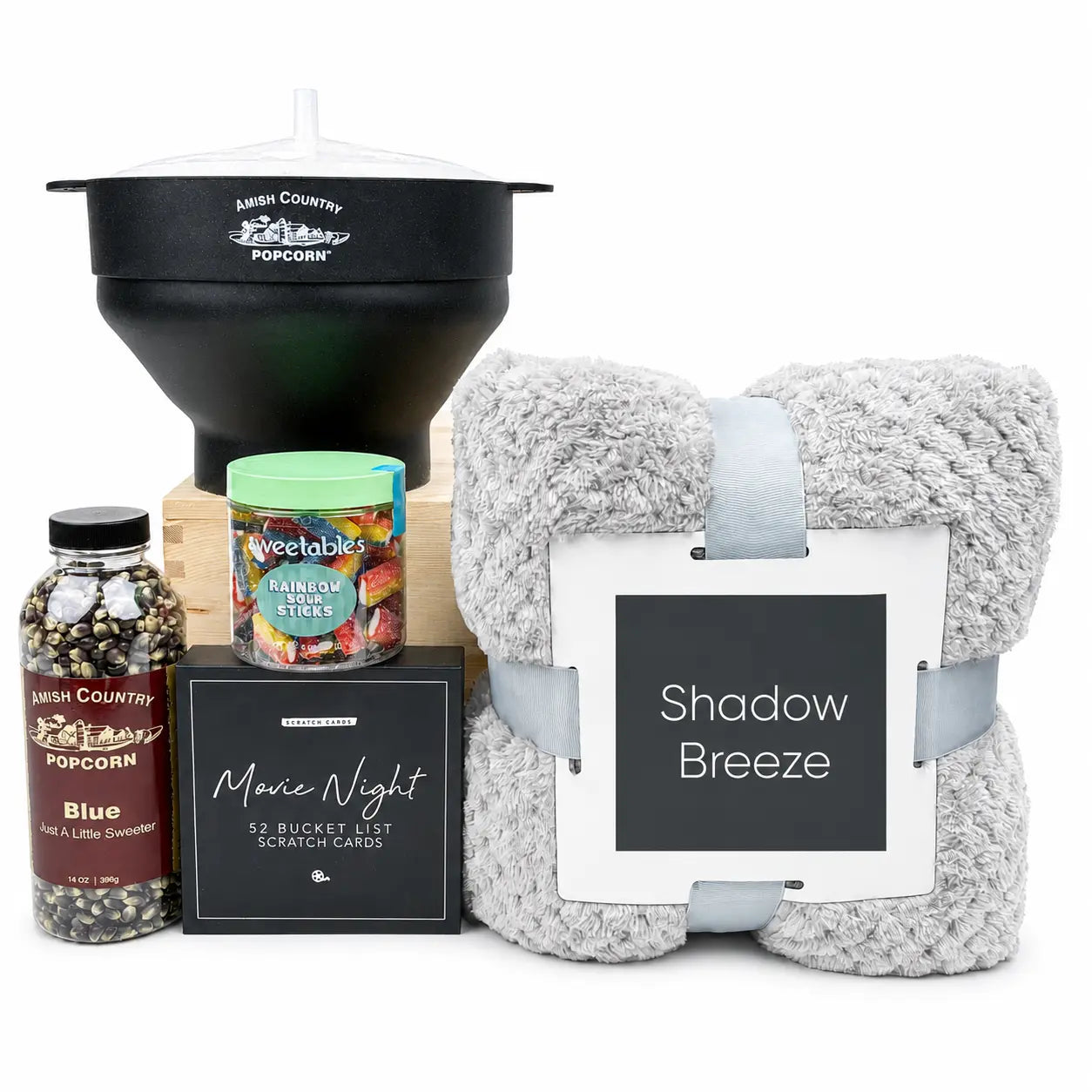 A curated gift basket set on a white background, featuring a black Mesh Country Popcorn funnel, a gray plush throw blanket with a white and gray 'Shadow Breeze' tag, a bottle of Mesh Country Blue Popcorn, a Vegtables snack jar, and a black 'Movie Night' scratch card box.