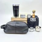 Grooming products including a black leather dopp kit, tumbler, and 'CRUX' branded items on a white background.
