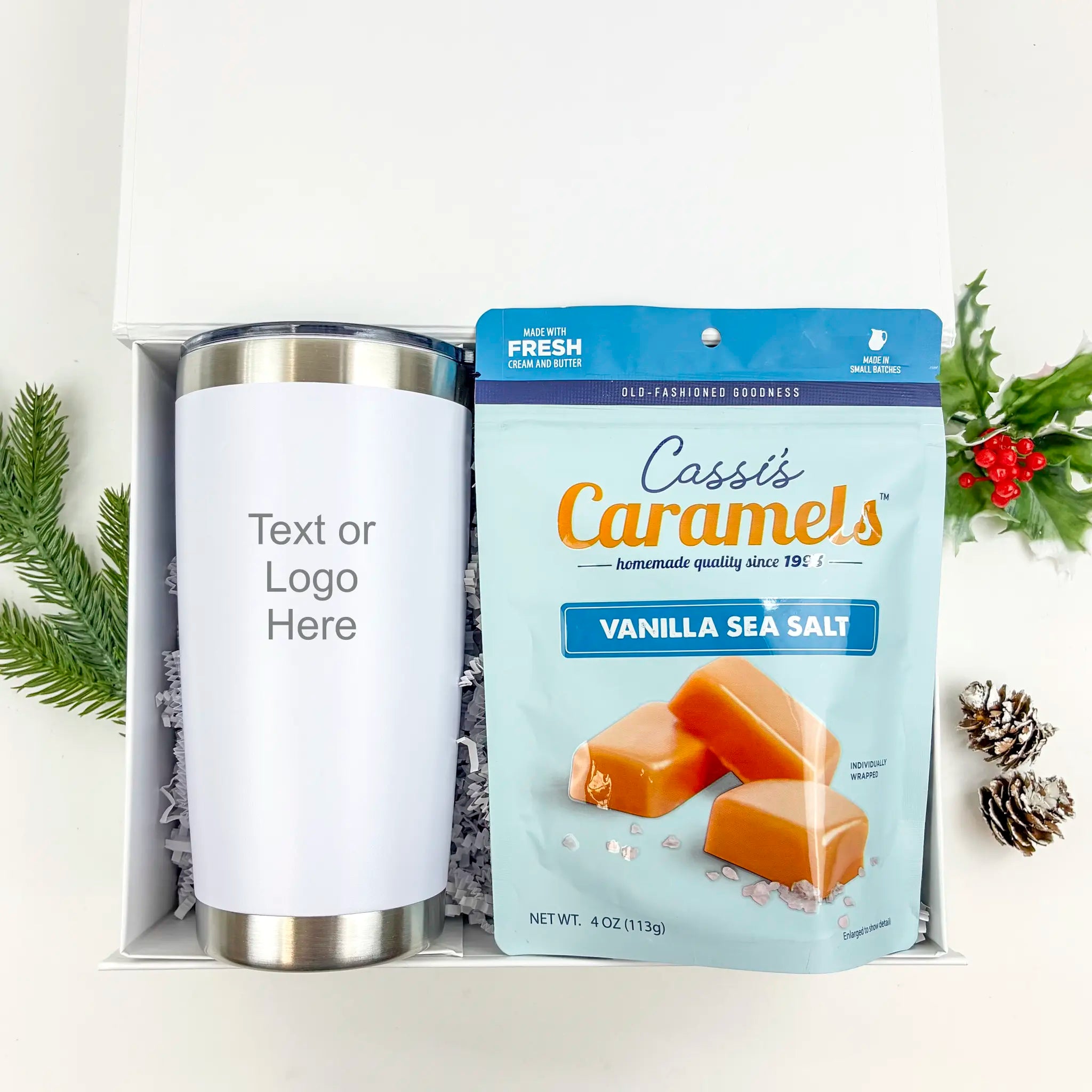 White tumbler and package of Cassi's Caramels Vanilla Sea Salt on a white background with Christmas decorations.