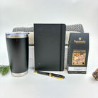 Black tumbler, notebook, pen, and cashew nut package on a white surface with a white background