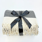 Blanket with black and white pattern and white fringe, tied with a black ribbon on a light gray background.