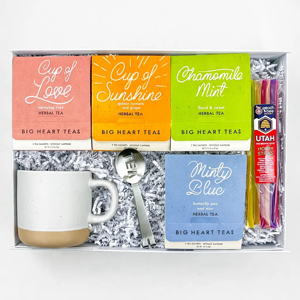 Tea gift set with tea boxes, mug, spoon, and honey sticks in a box.